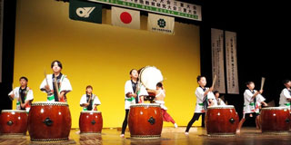 服部博之さん（中央後方）と太鼓のコラボ演奏をする滝之原小の児童たち＝津市の三重県総合文化センター